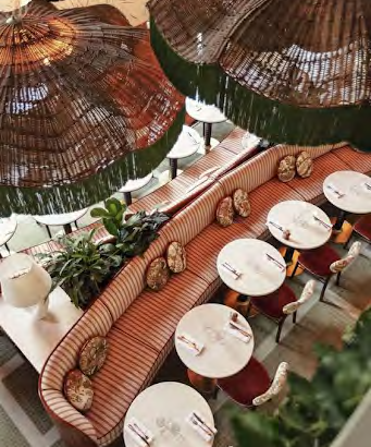 A chic cafe with curved red booths, white round tables, red chairs, and hanging wicker umbrellas creating a cozy outdoor dining vibe.