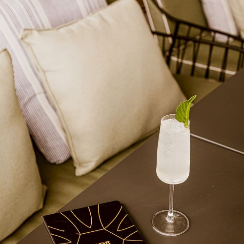 A lounge set with cushions, a glass cocktail topped with a mint leaf, and a ToppA gift box on a table.